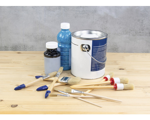 Kbelík s barvou, lahve s barvou a štětce na dřevěném stole