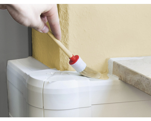 Ruka natírá kulatým štětcem barvu na zeď.