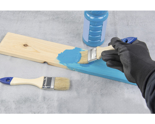 Osoba natírá dřevěnou desku štětcem a barvou.