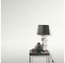 Světlá tapeta s texturou, stolní lampa, dekorace a stolek v pokoji.
