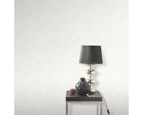 Světlá tapeta s texturou, stolní lampa, dekorace a stolek v pokoji.