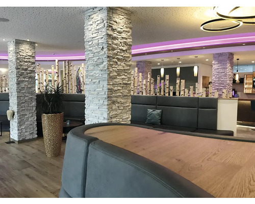 Interiér s kamennými sloupy, posezením a dřevěnými prvky.