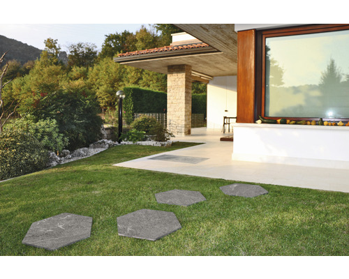 Zahradní chodník ze šestihranných kamenných desek v trávníku před moderním domem.