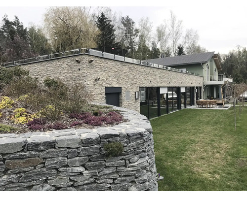 Vnější pohled na moderní dům s kamennou fasádou, zahradou a kamennou zídkou.