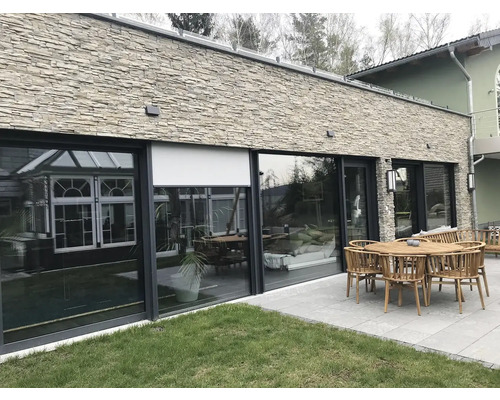 Fasáda domu s okenní stěnou, venkovní roletou a zahradním nábytkem