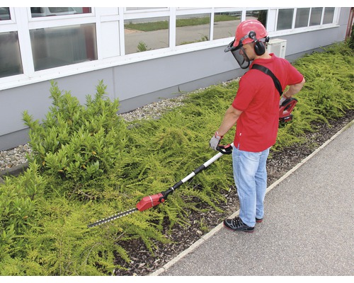 Muž stříhá živý plot akumulátorovými nůžkami na živý plot s teleskopickou tyčí a ochranným zařízením