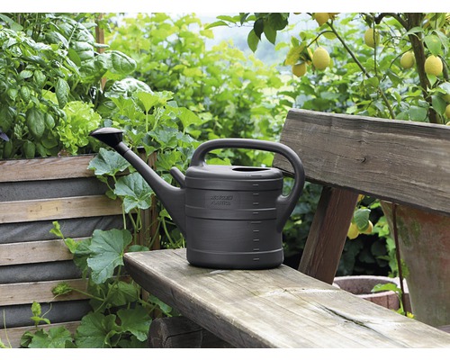 Plastová konev na zalévání na dřevěné lavici v zahradě