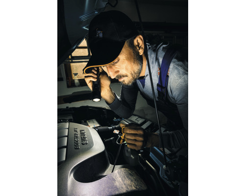 Muž kontroluje motorový prostor auta s baterkou.