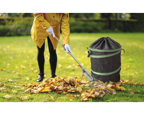 Žena uklízí listí hráběmi a zahradním pytlem