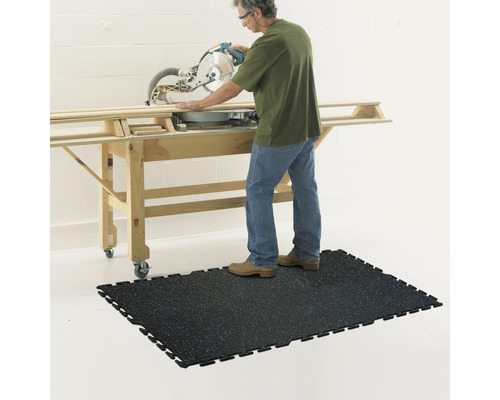 Osoba obsluhuje pokosovou pilu na pracovním stole a stojí na černé dílenské podložce.
