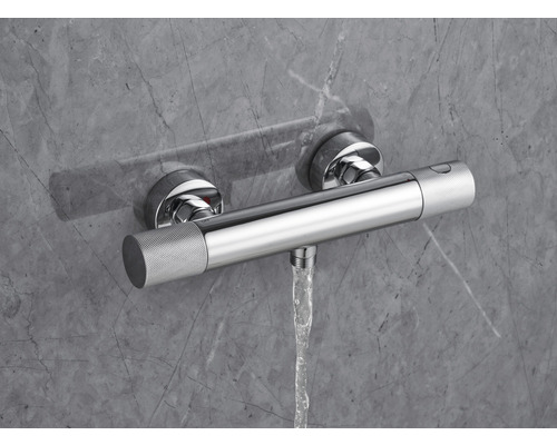 Termostatická baterie na omítku s proudem vody před šedou stěnou