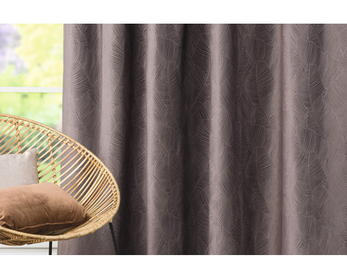 Dekorativní závěs s motivem listů vedle ratanového křesla