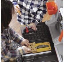 Dvě děti si hrají s pracovními stoly a nářadím.