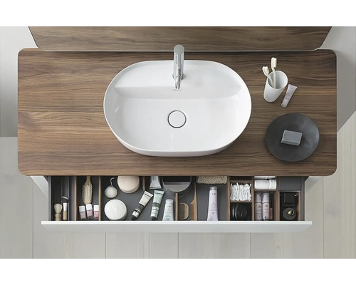 Snímek koupelny s umyvadlem na umyvadlové skříňce a otevřenou zásuvkou s toaletními potřebami