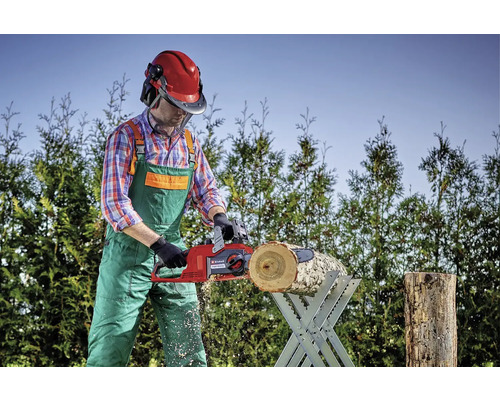 Osoba řeže kus dřeva na koze na řezání dřeva pomocí elektrické řetězové pily.