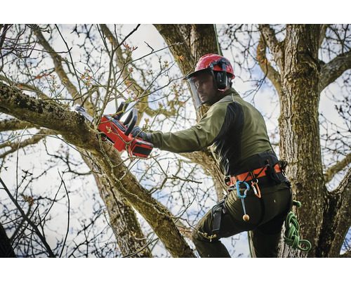 Arborista s helmou a ochranným oděvem pro řezání větví s akumulátorovou pilou.