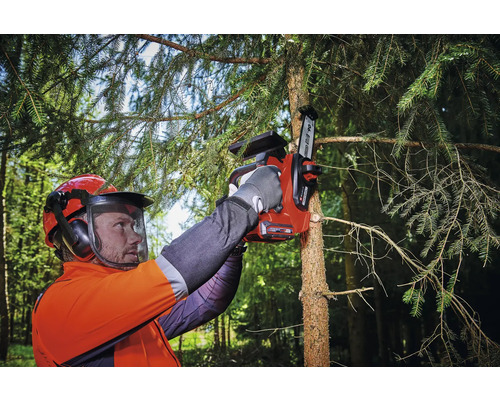 Osoba s bezpečnostním vybavením používá akumulátorovou pilu k řezání větve stromu.