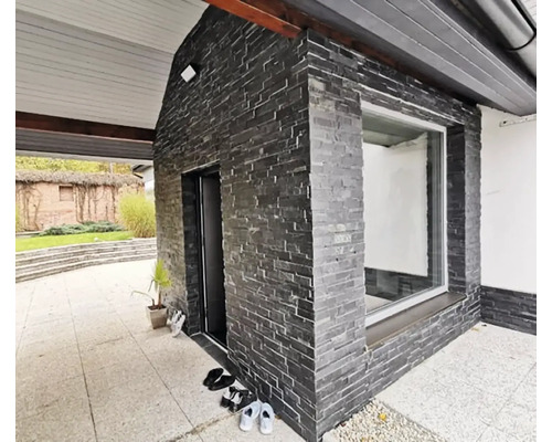 Fasáda s tmavými obkladovými kameny, okno a vchodové dveře.