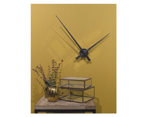 Dekorativní scéna s nástěnnými hodinami, zlatým květináčem a skleněnými krabicemi na stole.