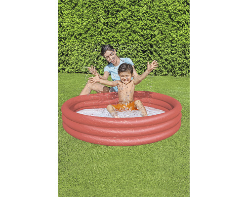 Matka a dítě si hrají v kulatém, červeném bazénku na zahradě.