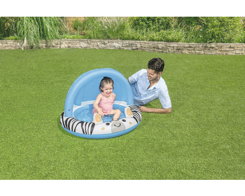 Nafukovací brouzdaliště se vzorem zebry a sluneční stříškou na zahradě s hrajícím si dítětem a dospělým