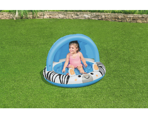 Dítě sedí v nafukovacím bazénku se vzorem zebry a sluneční ochranou
