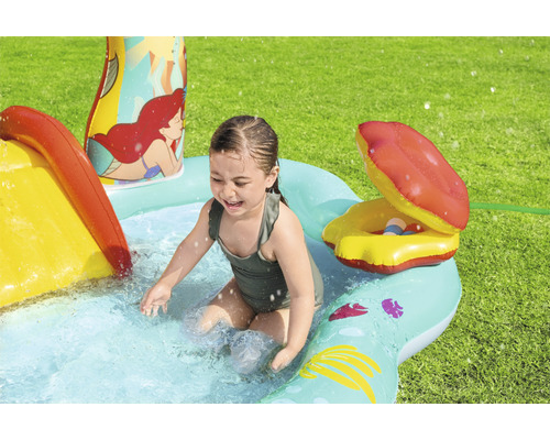 Dívka si hraje v nafukovacím brouzdališti se skluzavkou a vodním postřikovačem