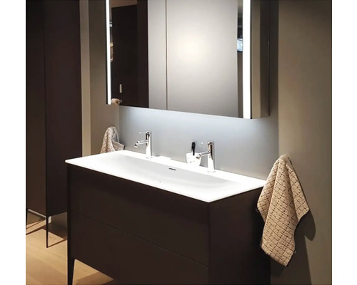 Moderní koupelna s dvojitým umyvadlem, osvětlenou zrcadlovou skříňkou a ručníky.