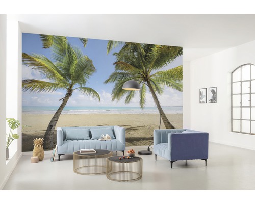 Obývací pokoj s fototapetou zobrazující tropickou scénu s palmami a pláží, s nábytkem, jako je pohovka a křesla.