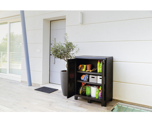 Zahradní skříňka s otevřenými dveřmi, plná zahradního nářadí před domem