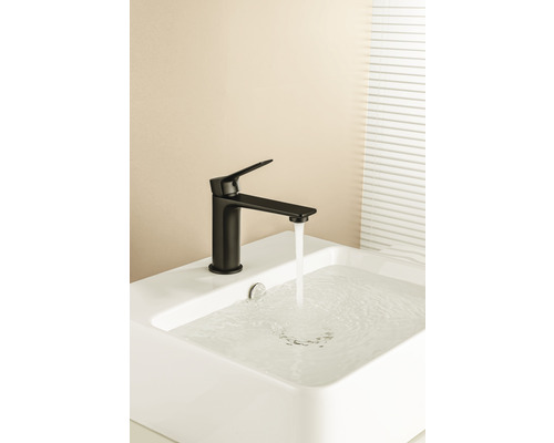 Černá armatura na bílém umyvadle s tekoucí vodou.