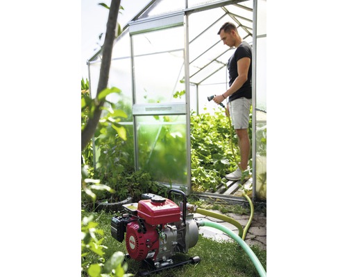 Motorové zahradní čerpadlo v provozu před skleníkem se zahradníkem