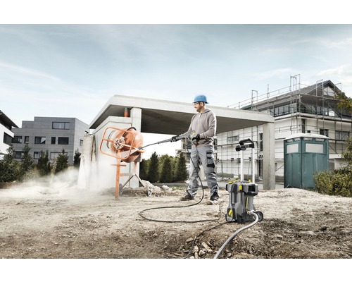 Muž čistí míchačku betonu vysokotlakým čističem na staveništi.