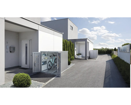 Box na kola před obytným domem s otevřenými dveřmi, uvnitř je kolo