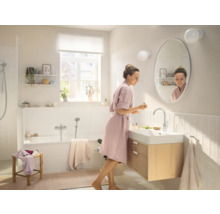 Světlá koupelna s vanou, skříňkou pod umyvadlo a ženou před zrcadlem