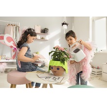 Dvě dívky si hrají v pokoji s rostlinou v květináči s obličejem a konví.