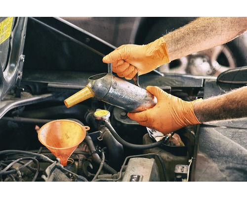 Osoba v rukavicích nalévá olej s nálevkou do motoru