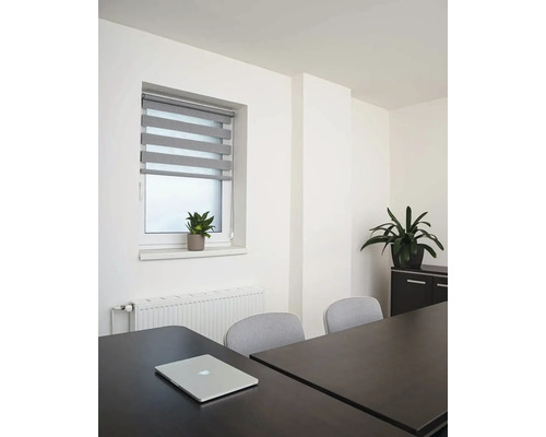 Světlá místnost s oknem, roletou, stolem a notebookem