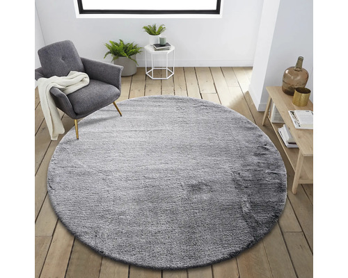 Kulatý šedý koberec v obývacím pokoji s křeslem a příručním stolkem.