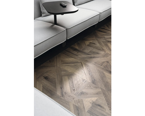 Detailní záběr místnosti s pohovkou, odkládacím stolkem a parketovou podlahou ve vzoru rybí kosti.