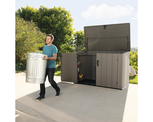 Muž nese popelnici k zahradnímu úložnému boxu na zahradě.