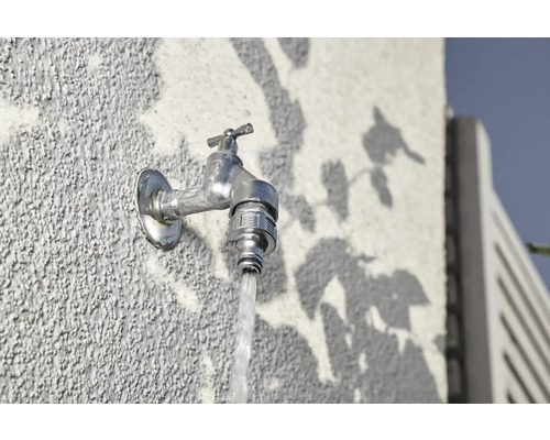 Venkovní vodovodní kohoutek na zdi s tekoucí vodou