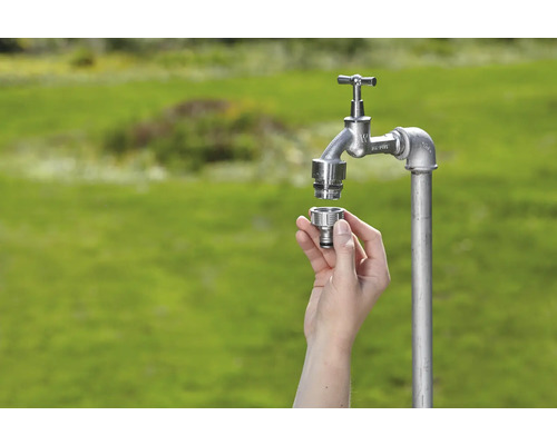 Venkovní vodovodní kohoutek s rychlospojkou v ruce na zeleném pozadí