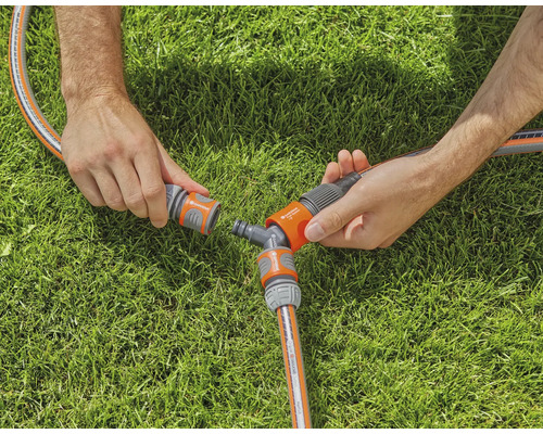 Dvě ruce spojují zahradní hadici s Y-rozbočovačem na trávníku.