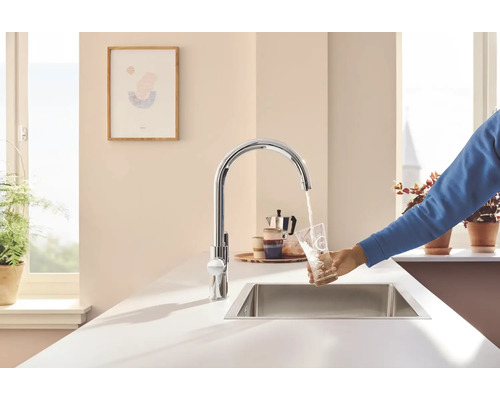 Kuchyňská scéna s dřezovou baterií, dřezem a osobou napouštějící sklenici vody