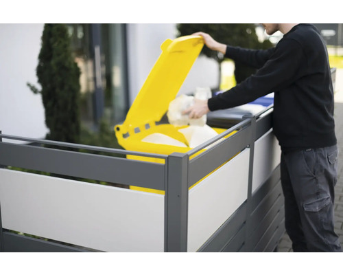 Osoba vyhazuje odpad do žluté popelnice za zástěnou