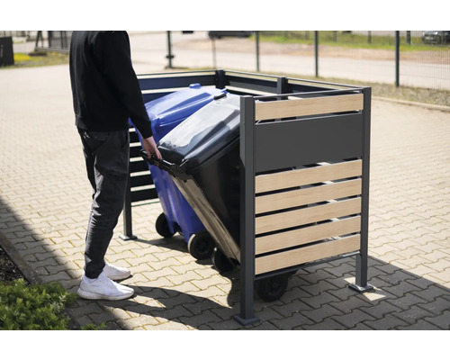 Osoba zasouvá popelnici do kovového a dřevěného boxu na popelnice