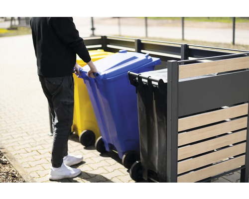 Osoba zasouvá modrou popelnici do boxu na popelnice