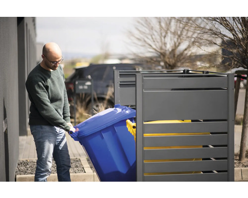 Osoba vkládá modrou popelnici do šedé skříně na popelnice.