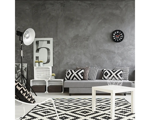 Obývací pokoj se šedou stěnou, pohovka s polštáři, koberec s geometrickým vzorem a bílý konferenční stolek.